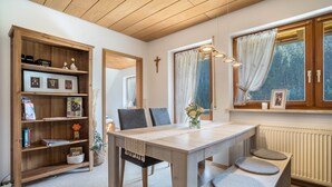 A dining area with a wooden table, chairs, a bench, a bookshelf, and a window with curtains. - Apartment Morgensonne, 55 sqm, 2 bedrooms, max. 4 persons (Hofstetten)