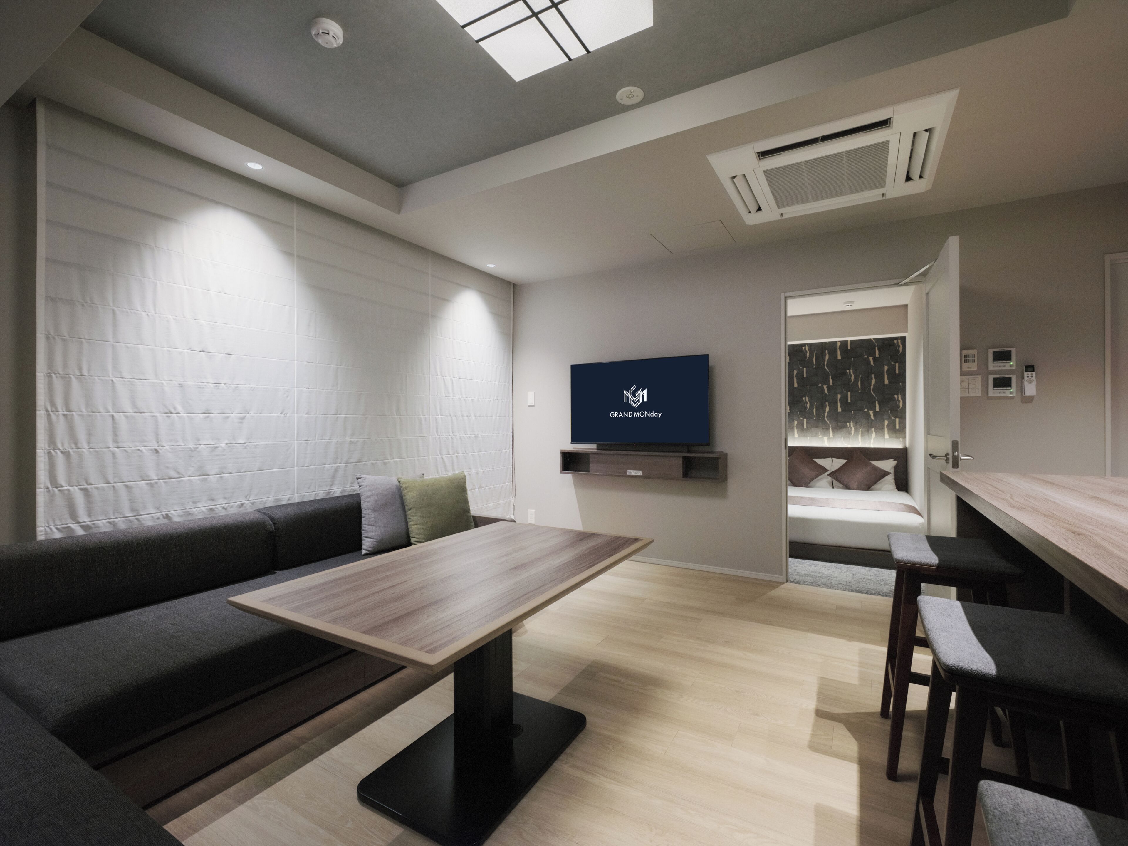 A modern hotel room with a sofa, a wooden table, a TV, a bed, and a bathroom.