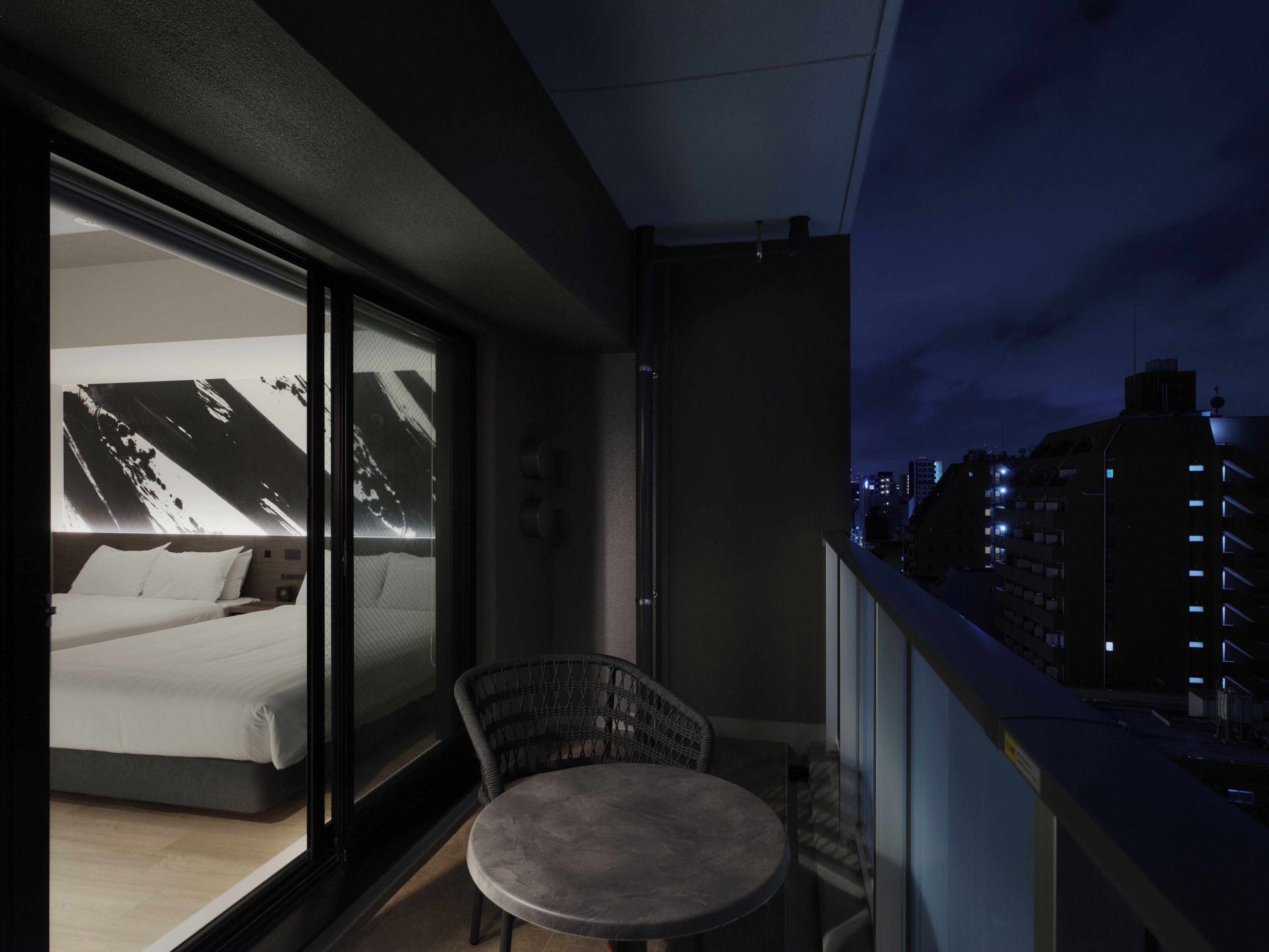 Un balcón con una cama y una mesa redonda, con vistas a un paisaje urbano nocturno.