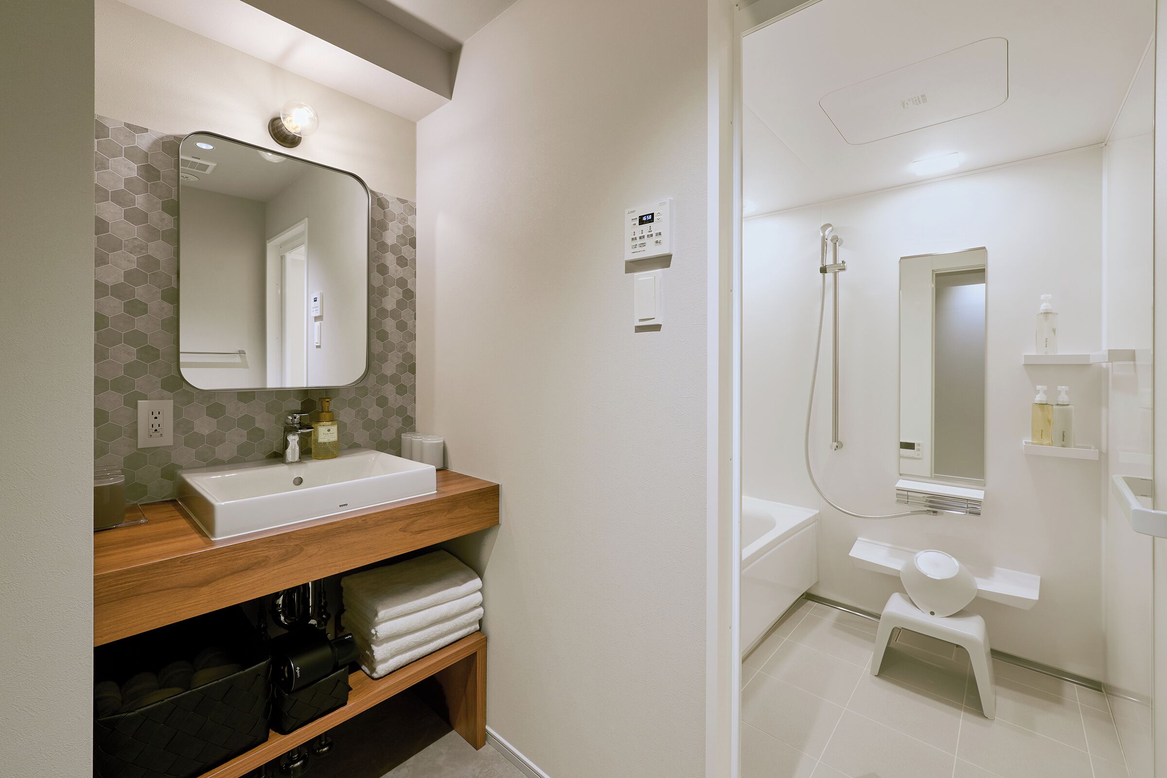 A modern bathroom with a wooden vanity, a large mirror, a shower area, and a small stool.