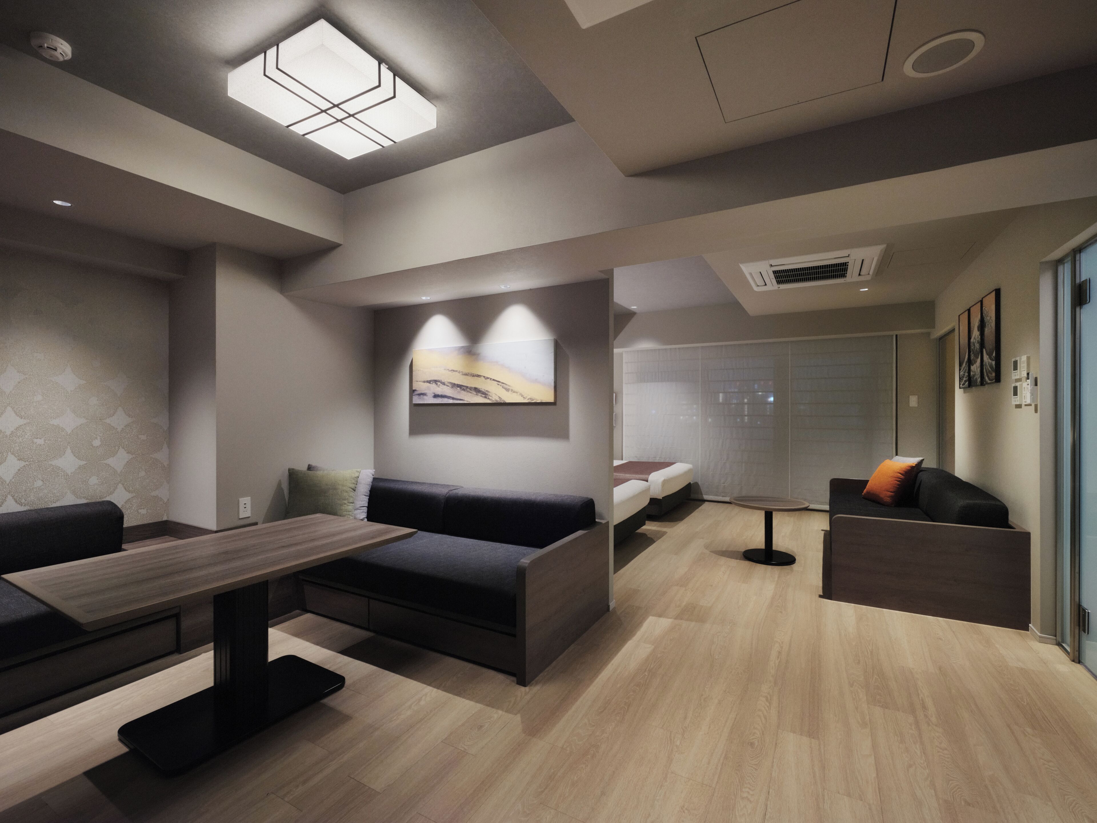 A modern hotel room with a sofa, a small table, a bed, and a bathroom with a shower.