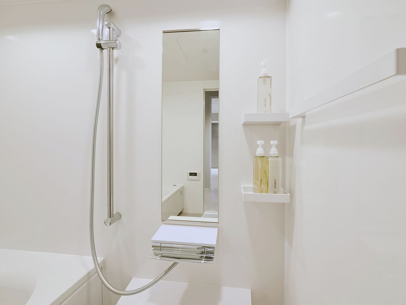 Une salle de bain moderne équipée d’une douche, d’un miroir et d’une étagère où sont rangés les articles de toilette.