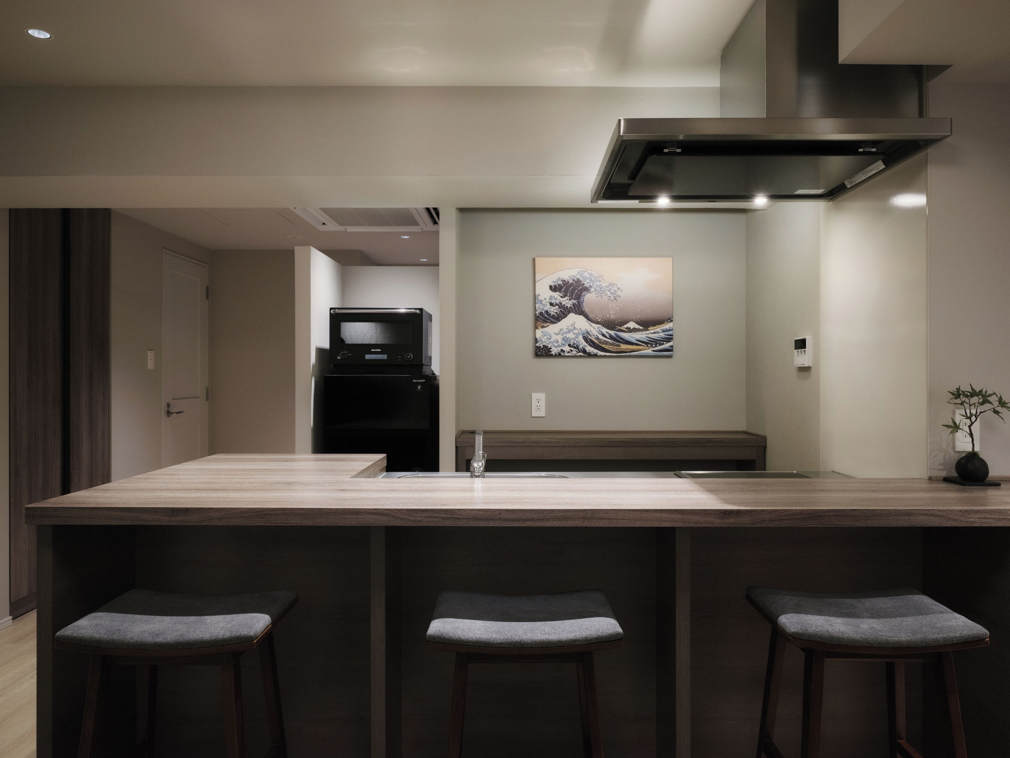 A modern kitchen with a central island, bar stools, a microwave, and a painting on the wall.