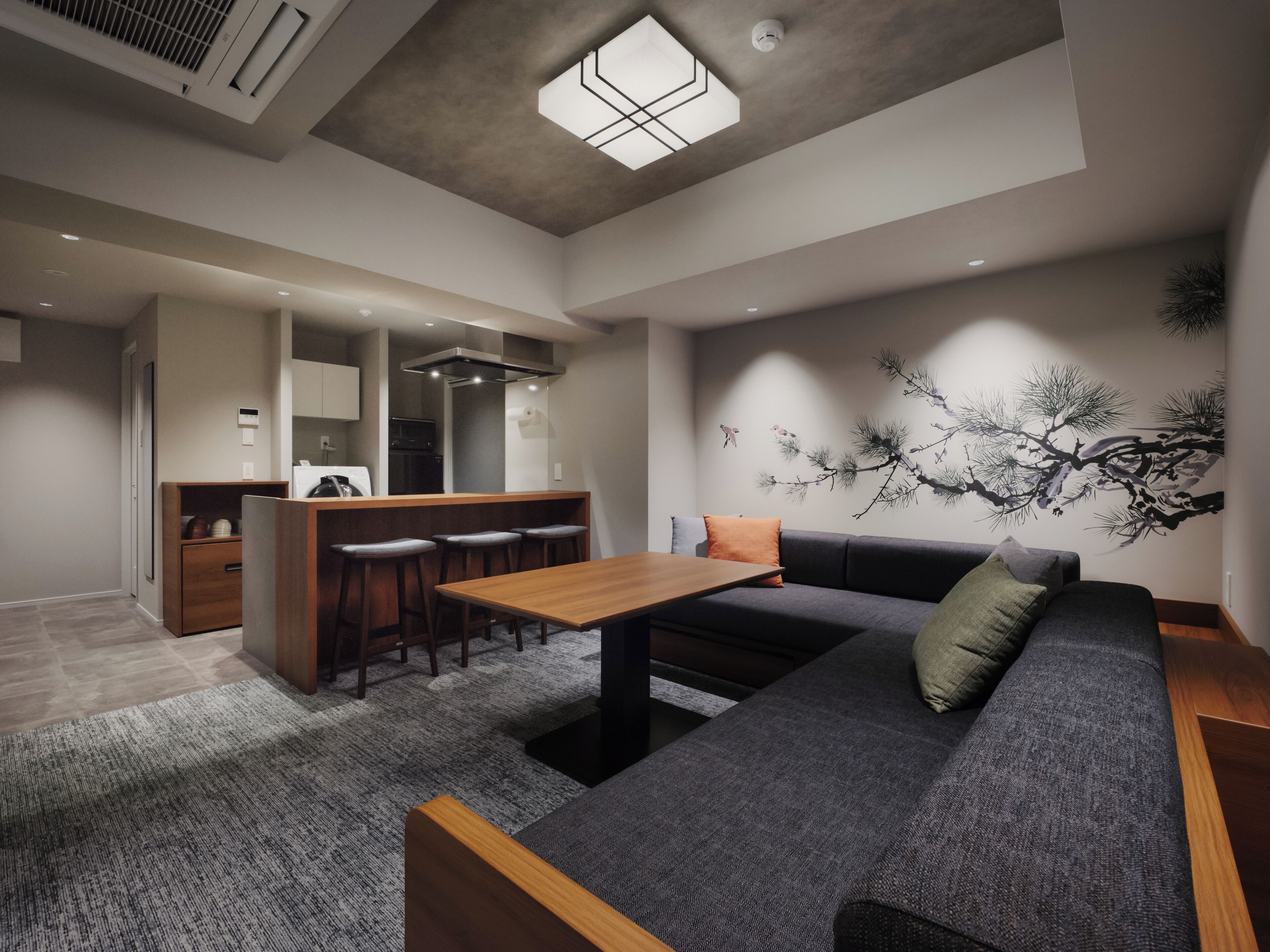 A modern living space with a kitchen, dining area, and a large gray sofa with a wooden table.