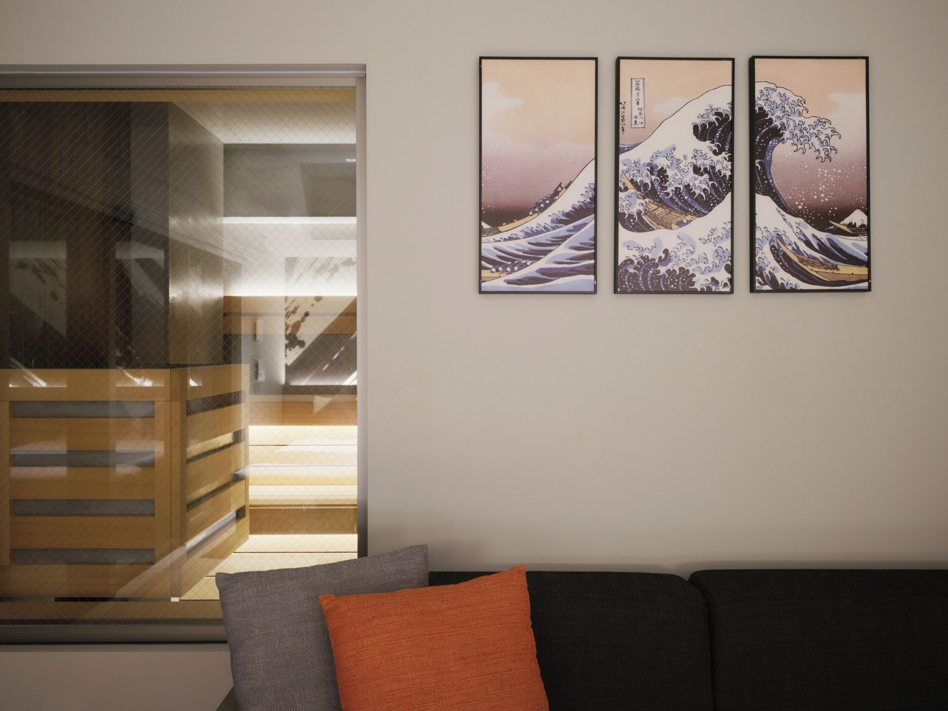 A room with a sliding door, a sofa with cushions, and three framed artworks on the wall.