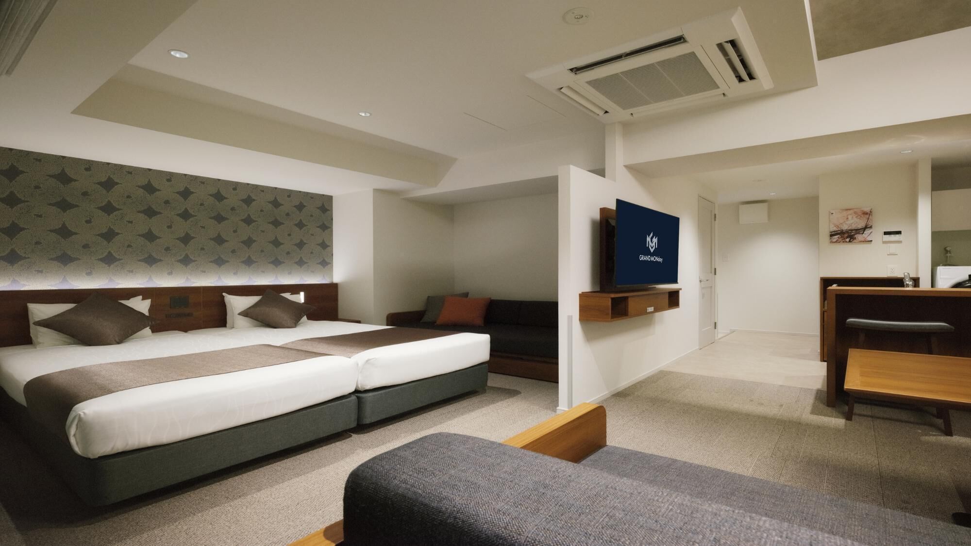 A modern hotel room with a double bed, a sofa, a desk, and a TV.