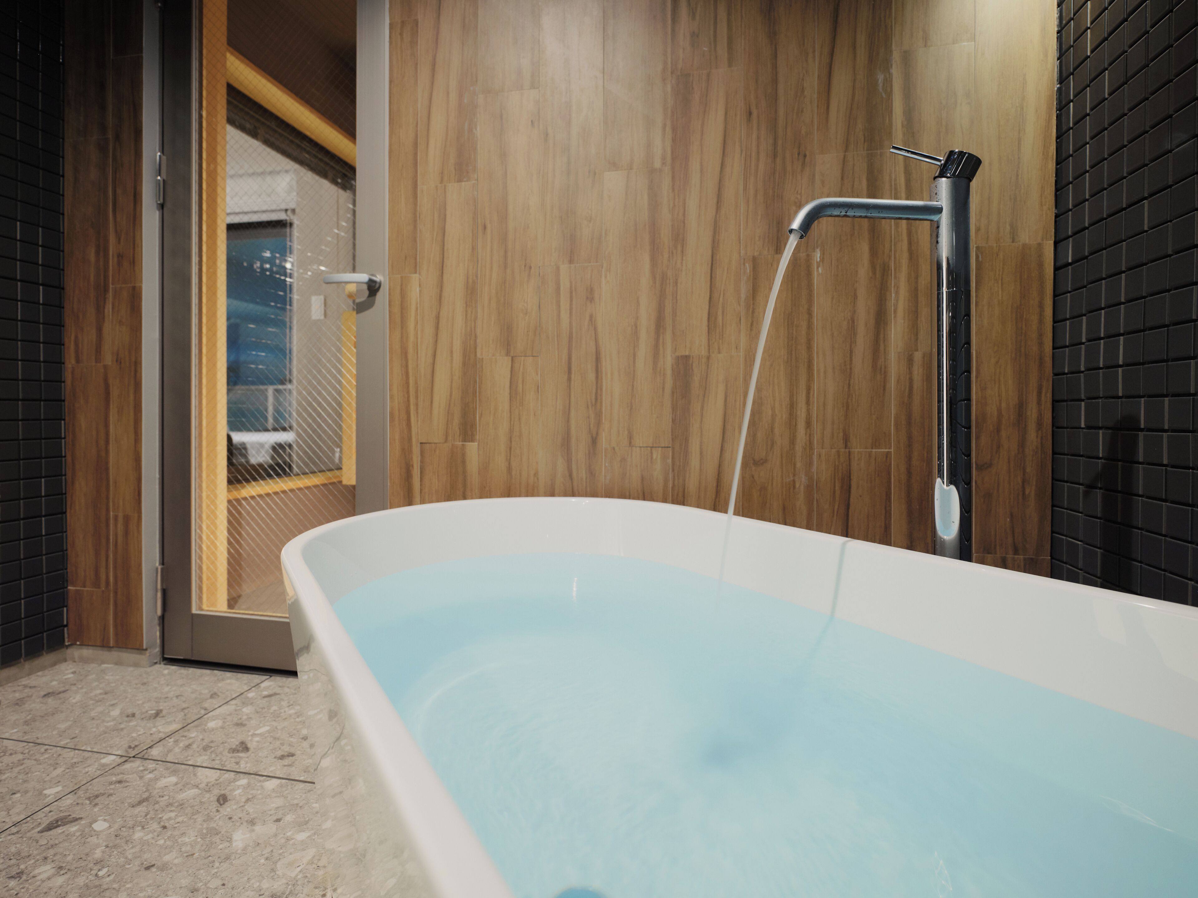 Une salle de bain moderne avec une baignoire sur pieds, un lambris mural en bois et un carrelage au sol.