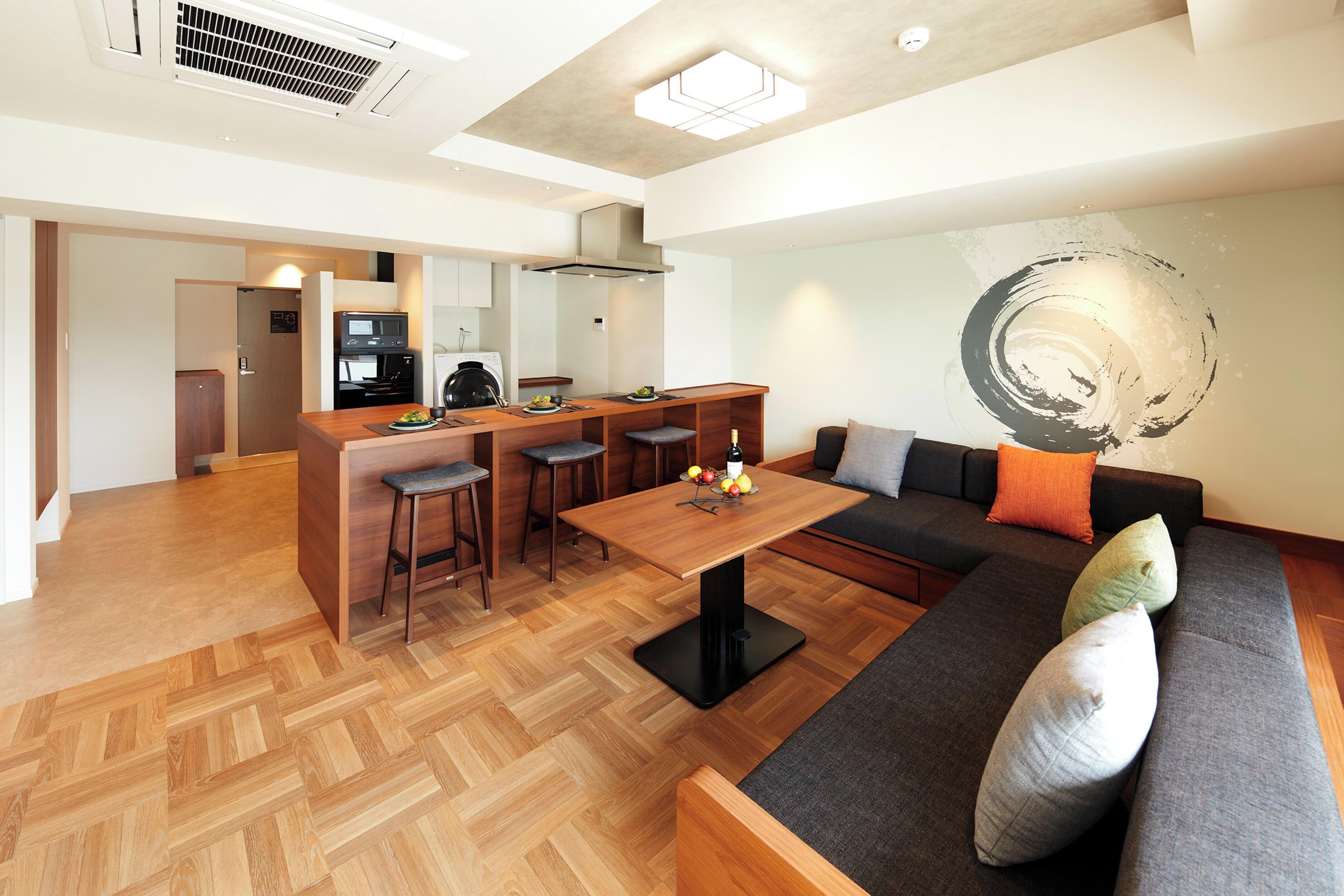 A modern living space with a wooden dining table, a sofa, and a kitchen area in the background.
