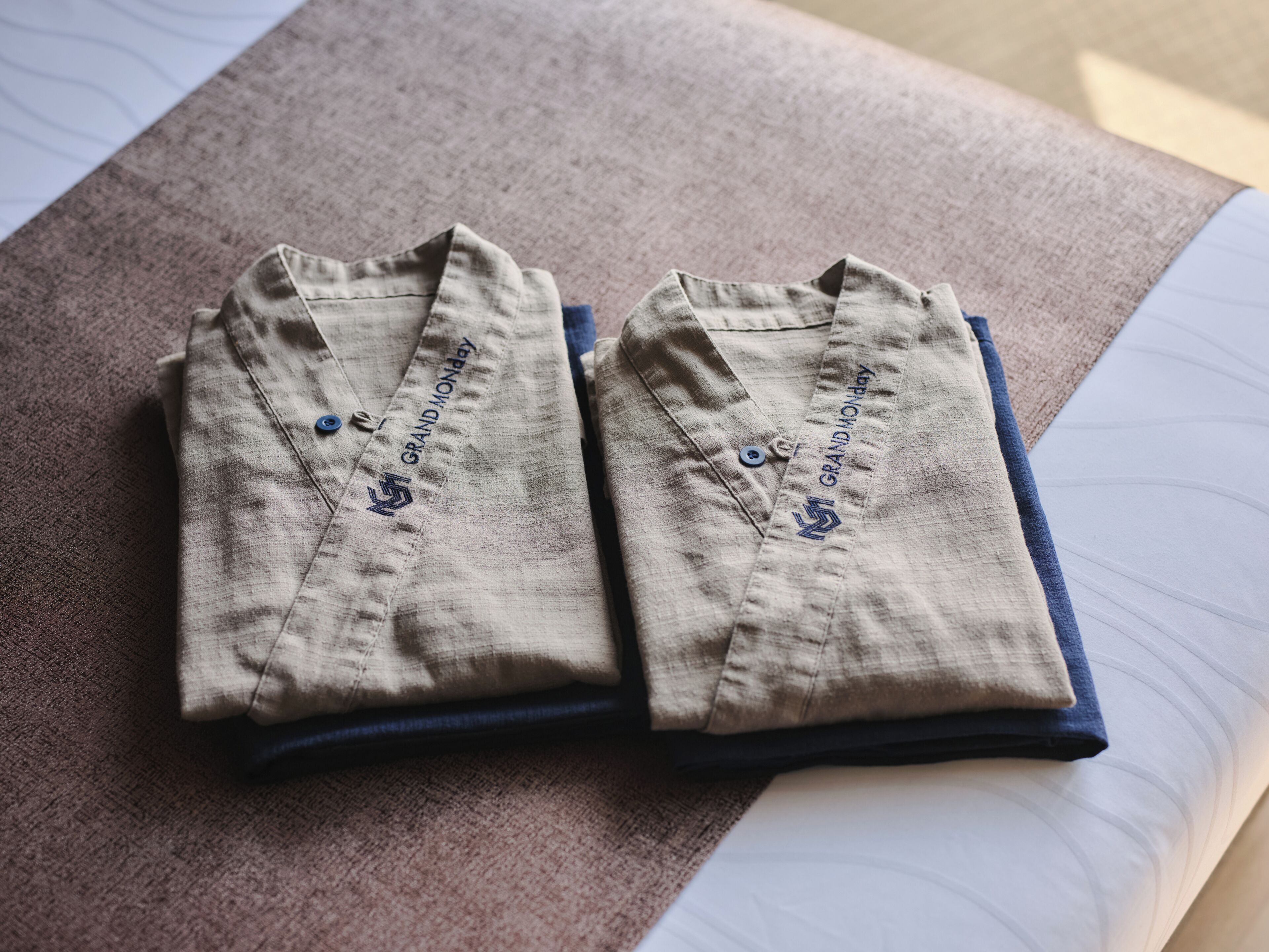 Two folded shirts with embroidery on the collar, placed on a bed with a visible sheet.
