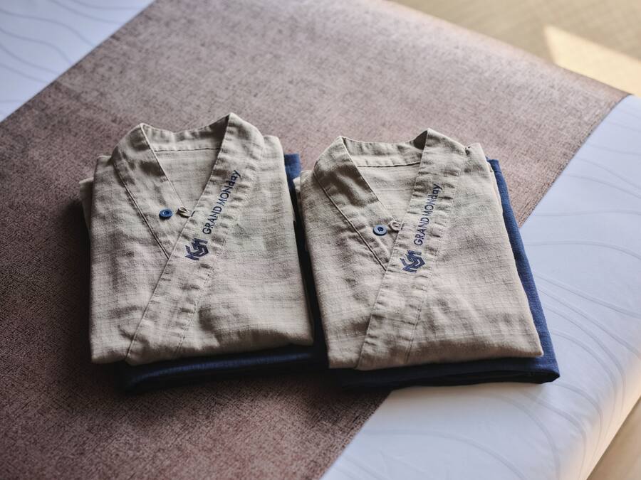 Two folded shirts with embroidery on the collar, placed on a bed with a visible sheet.