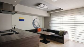 A modern kitchen with a built-in island, a dining area with a table and chairs, a sofa, and a large window with blinds.