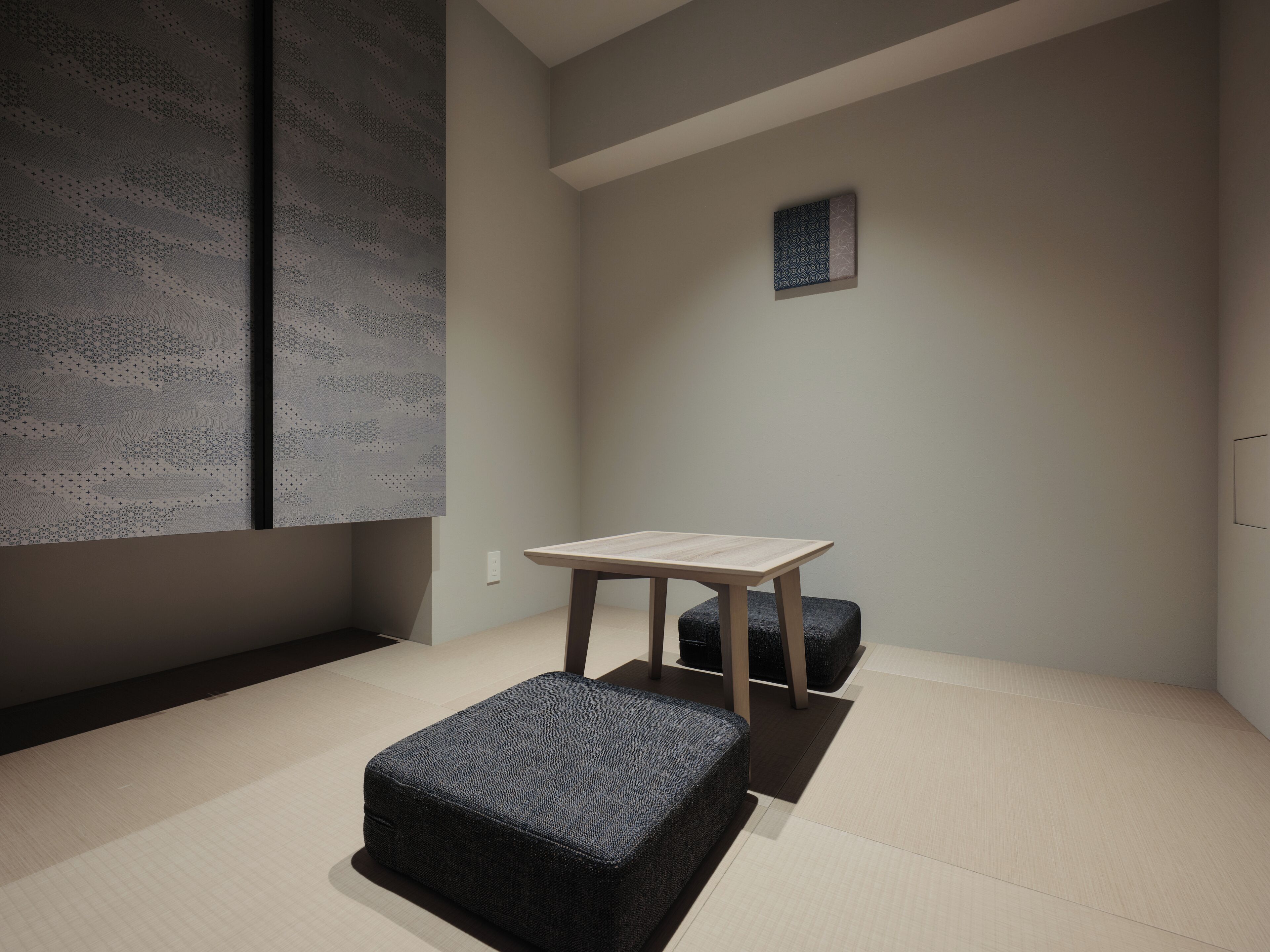 Ein schlicht eingerichteter Raum mit Tatami-Boden, einem niedrigen Holztisch und einem dunkelgrauen Ottomanen.