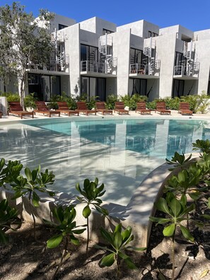 A modern hotel with a swimming pool, wooden lounge chairs, and a clear blue sky. - Tulum Sweet condo with private pool.  Enjoy nature in the Maya jungle! (Tulum)