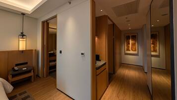 Habitación de hotel con piso de madera, un escritorio con teléfono, un banco y una lámpara fijada a la pared.
