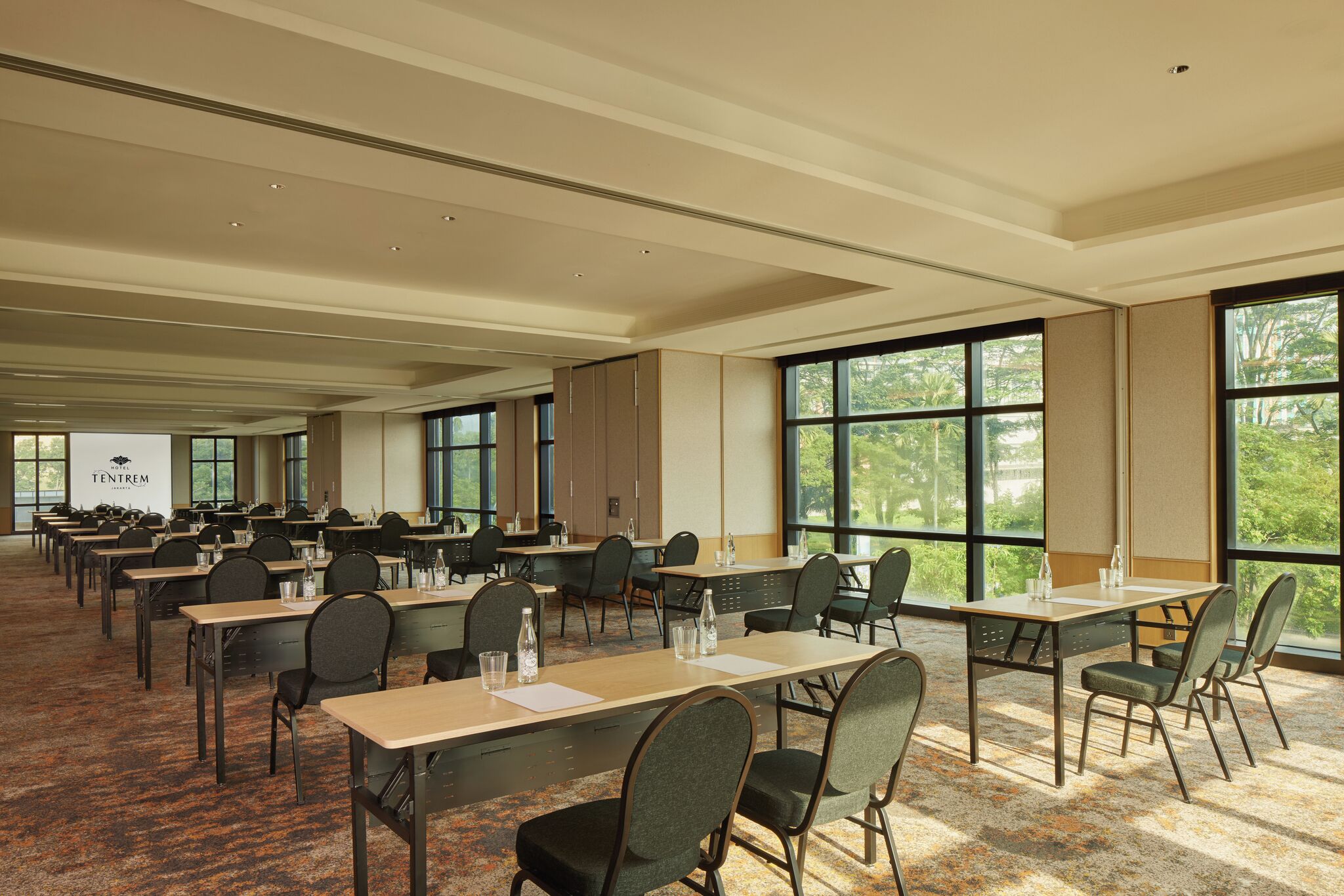 A large conference room with multiple tables and chairs, large windows with a view of trees, and a sign reading "TENTREM".