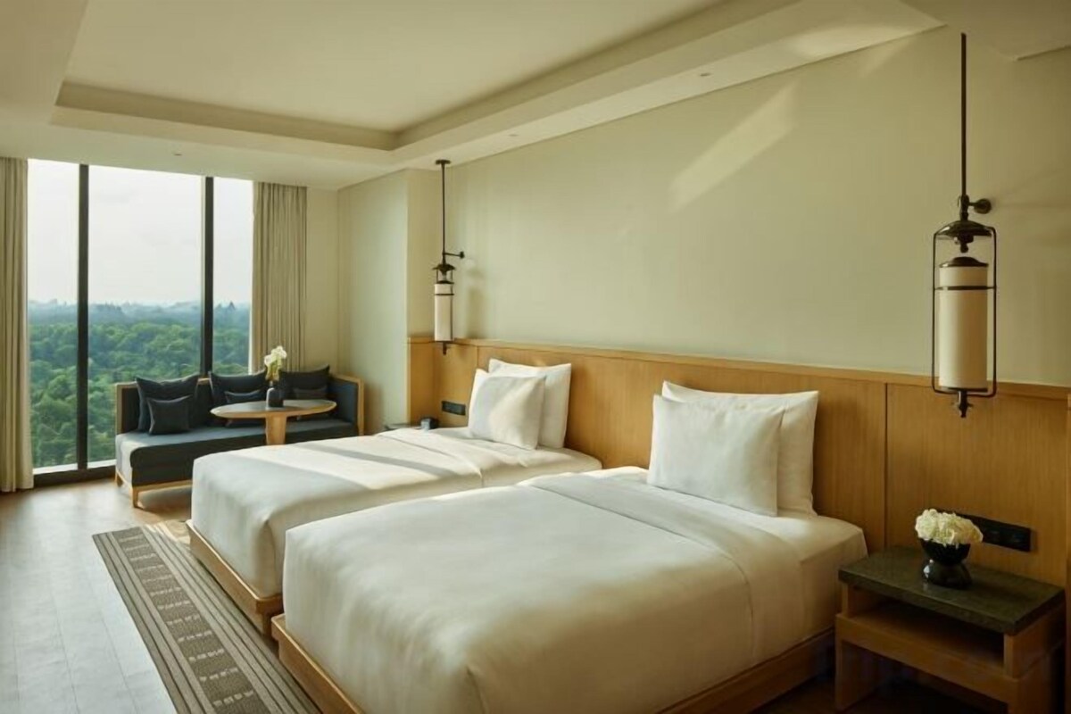 A hotel room with two beds, a sofa, a small table, and a view of the outdoors.