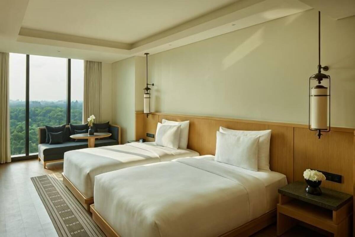 A hotel room with two beds, a sofa, a small table, and a view of the outdoors.