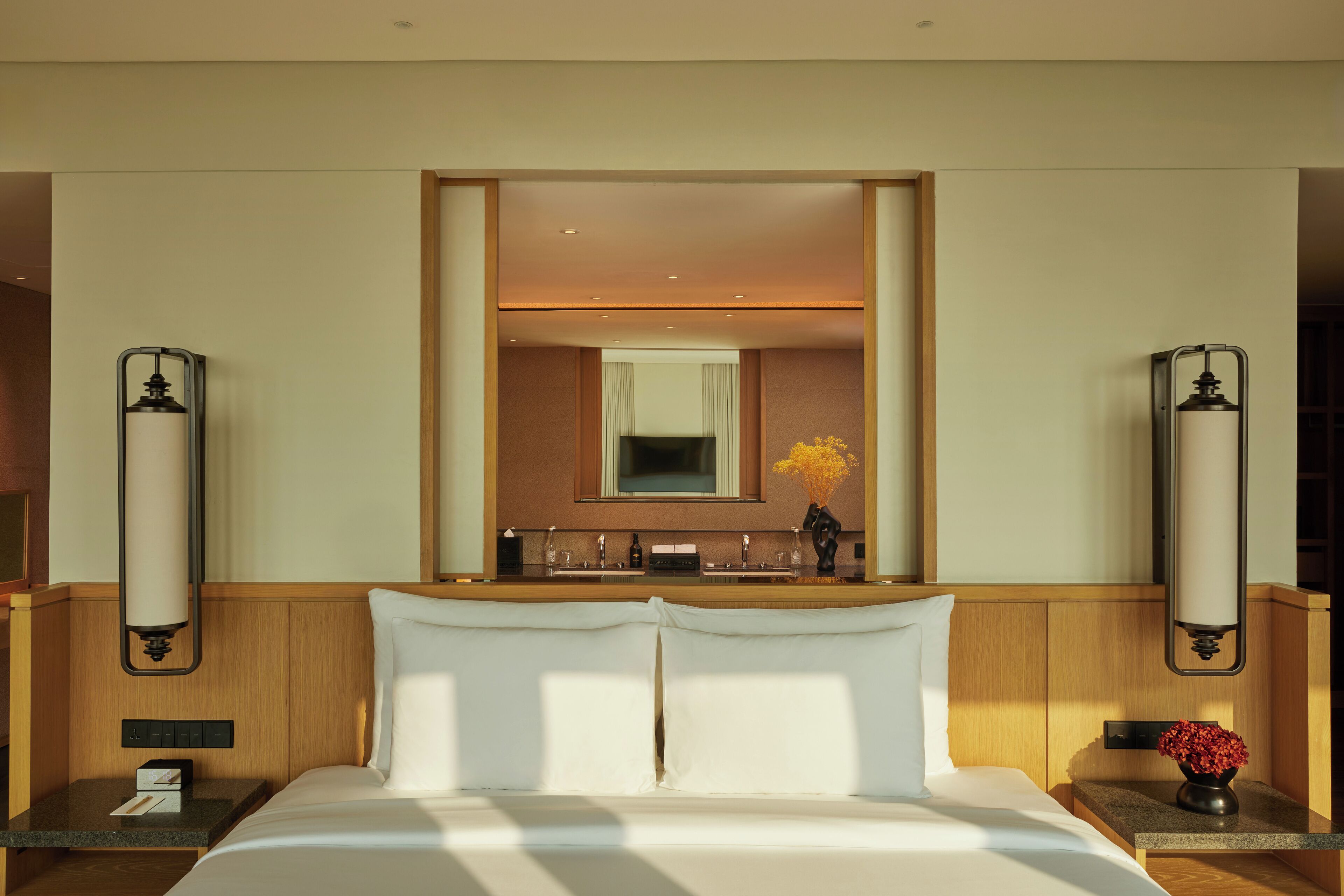 A hotel room with a large bed, a bedside table with a vase of flowers, a nightstand with a lamp, and a mirror above the dresser.