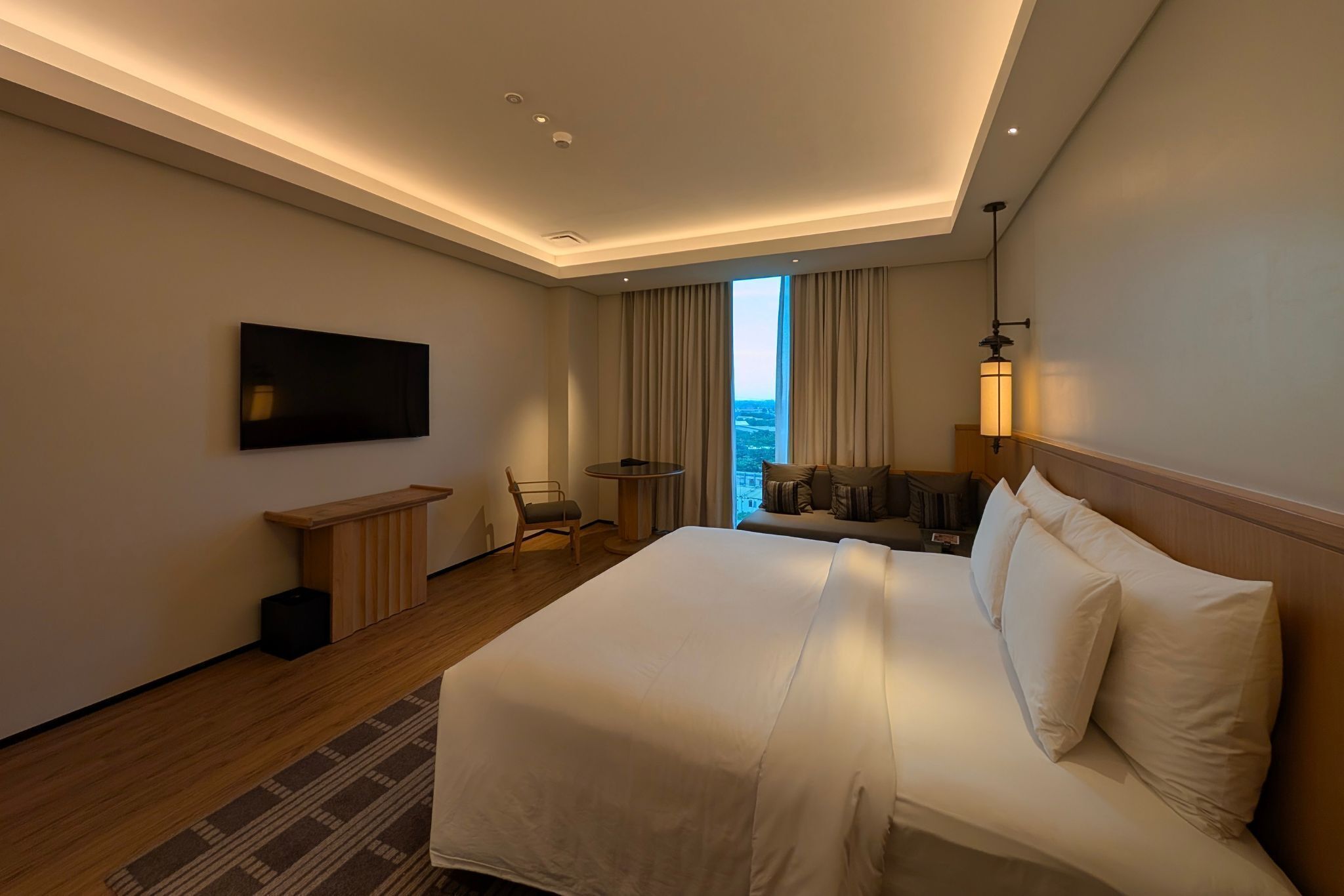 A hotel room with a large bed, a TV mounted on the wall, a small table, and a chair.