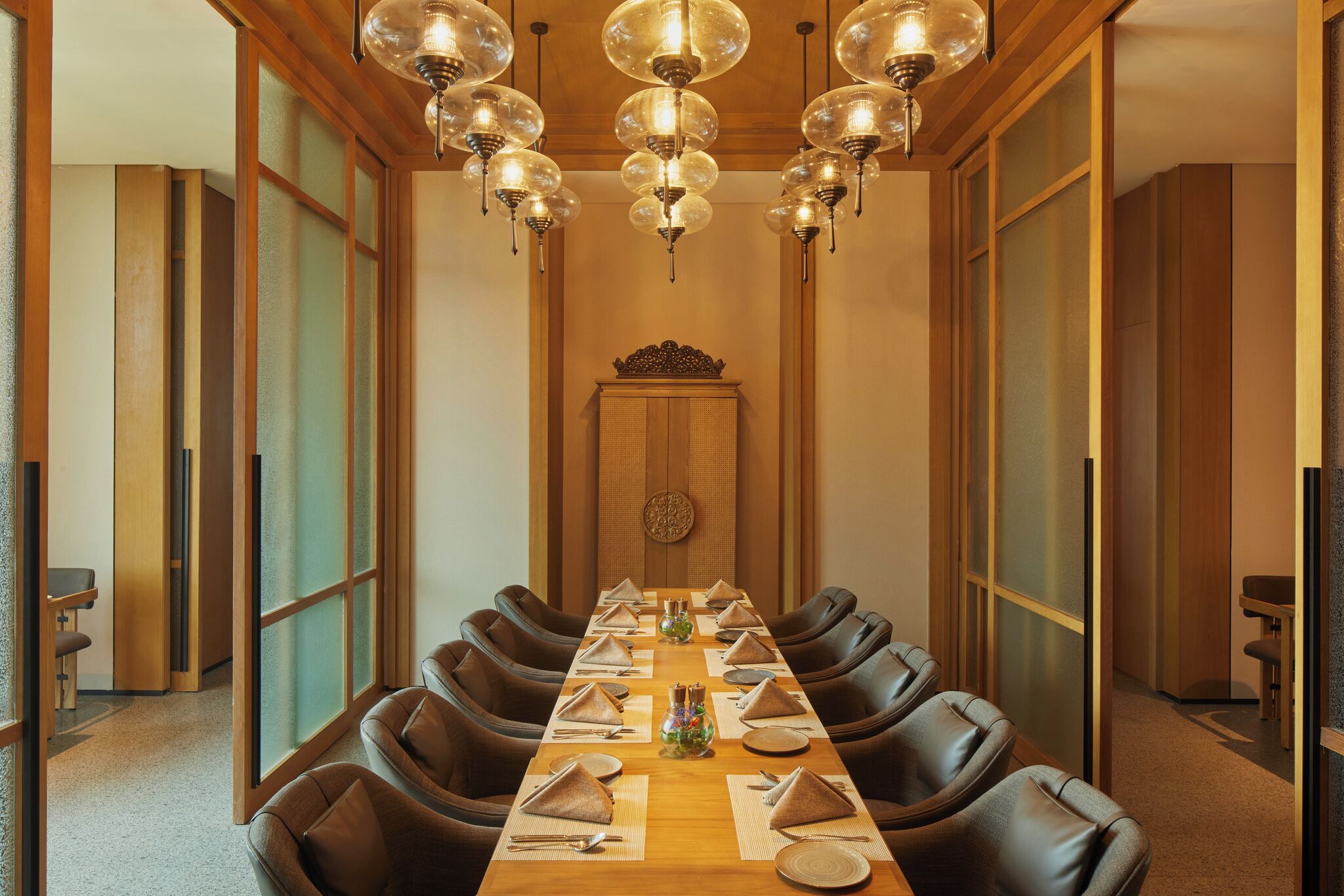 A conference room with a long table set for a meeting, surrounded by leather chairs, and a traditional Japanese-style ceiling light fixture.