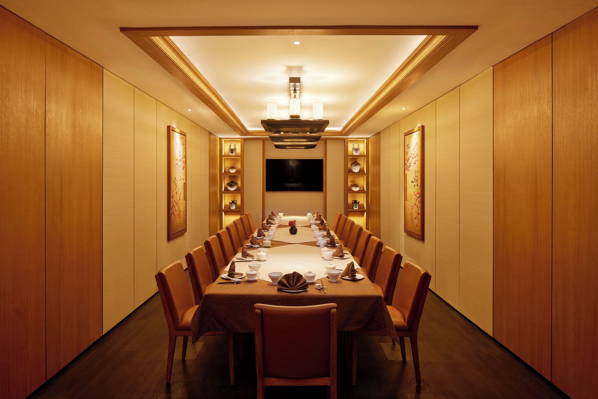 A long dining table with chairs, a chandelier, and wall-mounted shelves with decorative items.