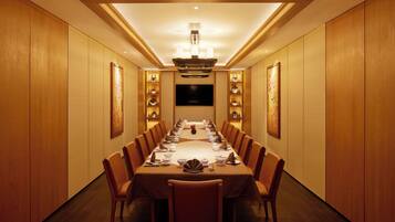 A long dining table with chairs, a chandelier, and wall-mounted shelves with decorative items.