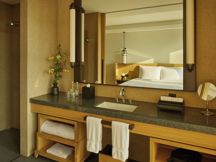 A hotel bathroom with a granite countertop, a sink, a mirror, a towel rack, and a shower area.