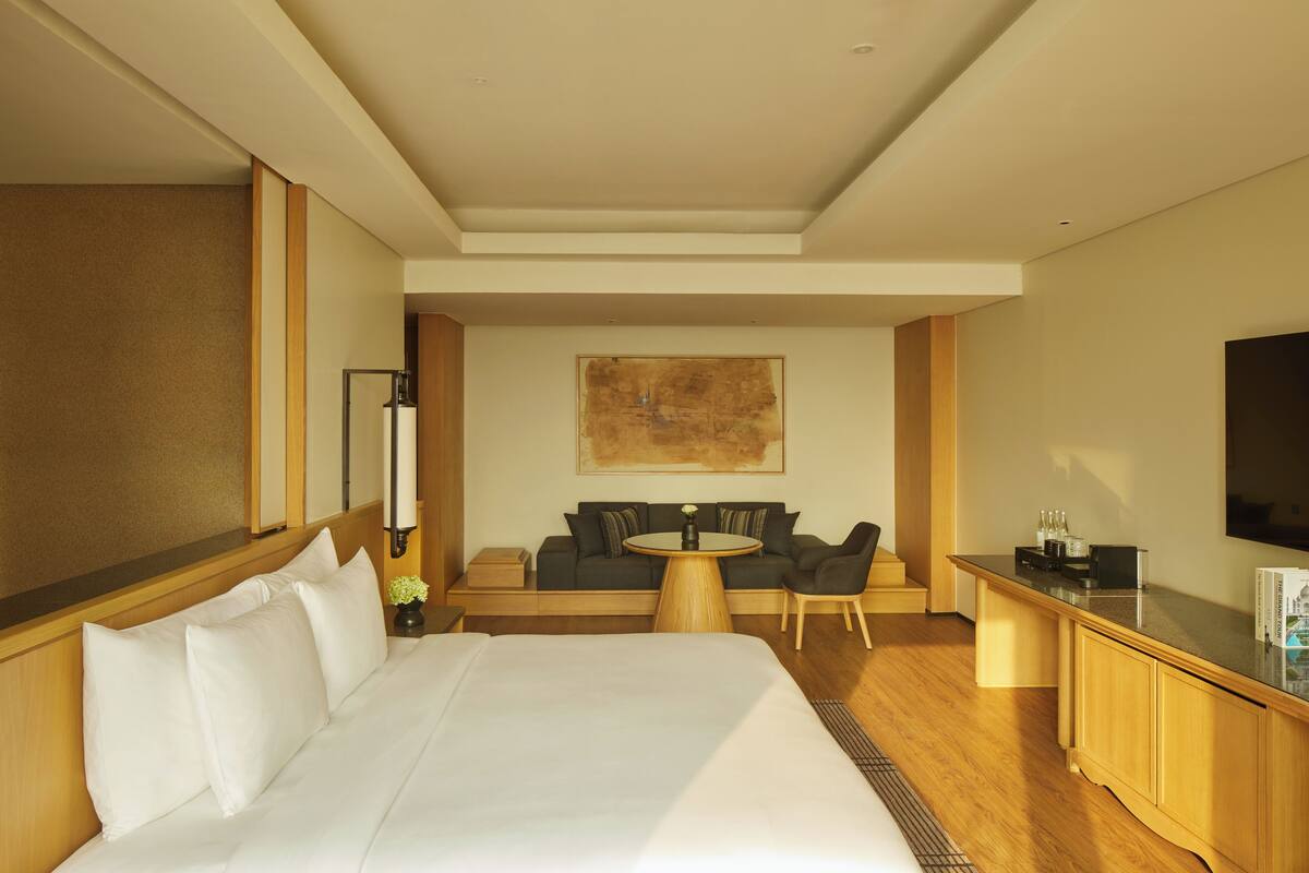 A hotel room with a large bed, a sofa, a small round table, a TV, and a wooden cabinet.