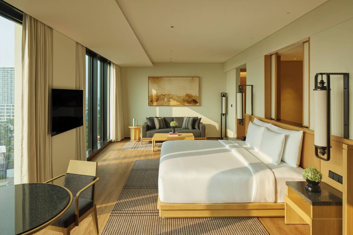 A hotel room with a large bed, a TV, a sofa, and a dining table.