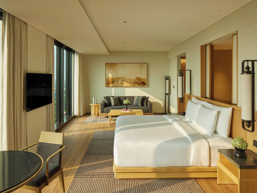 A hotel room with a large bed, a TV, a sofa, and a dining table.