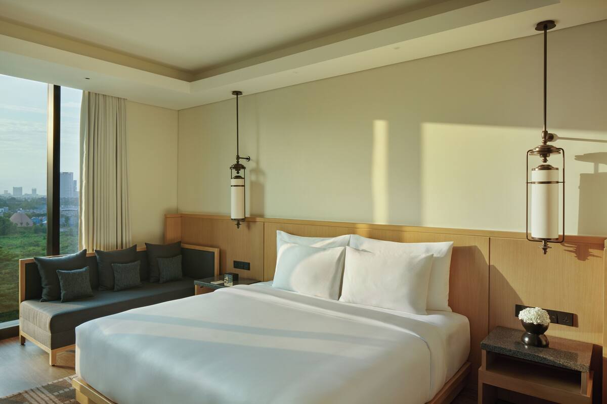 A hotel room with a large bed, a sofa, a nightstand, and a view of the city.