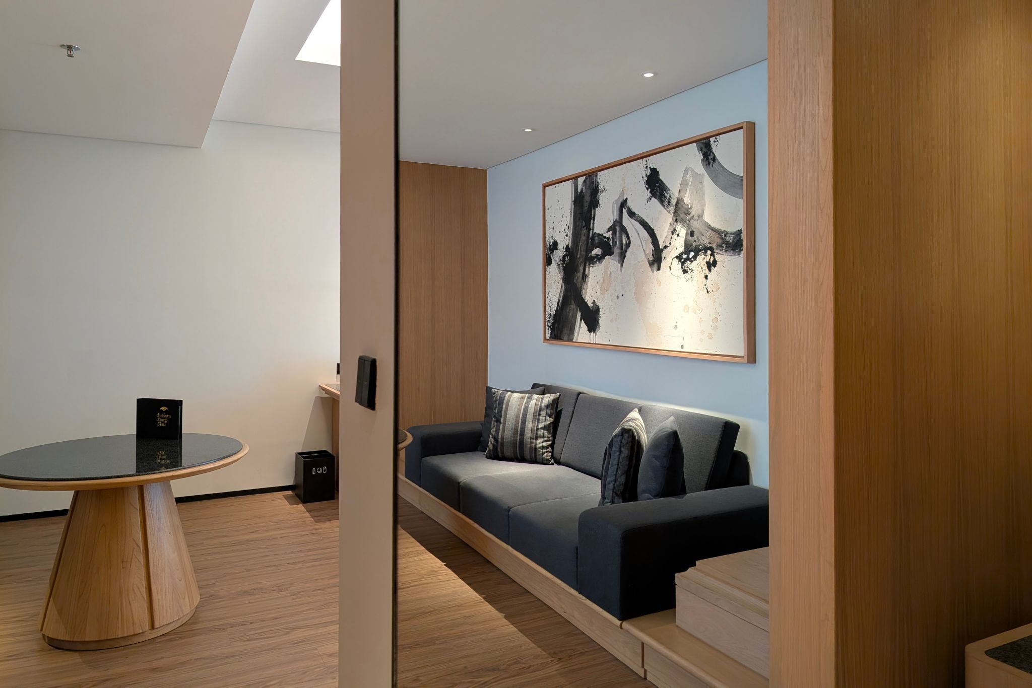 A modern room with a round table, a sofa, and a large abstract painting on the wall.