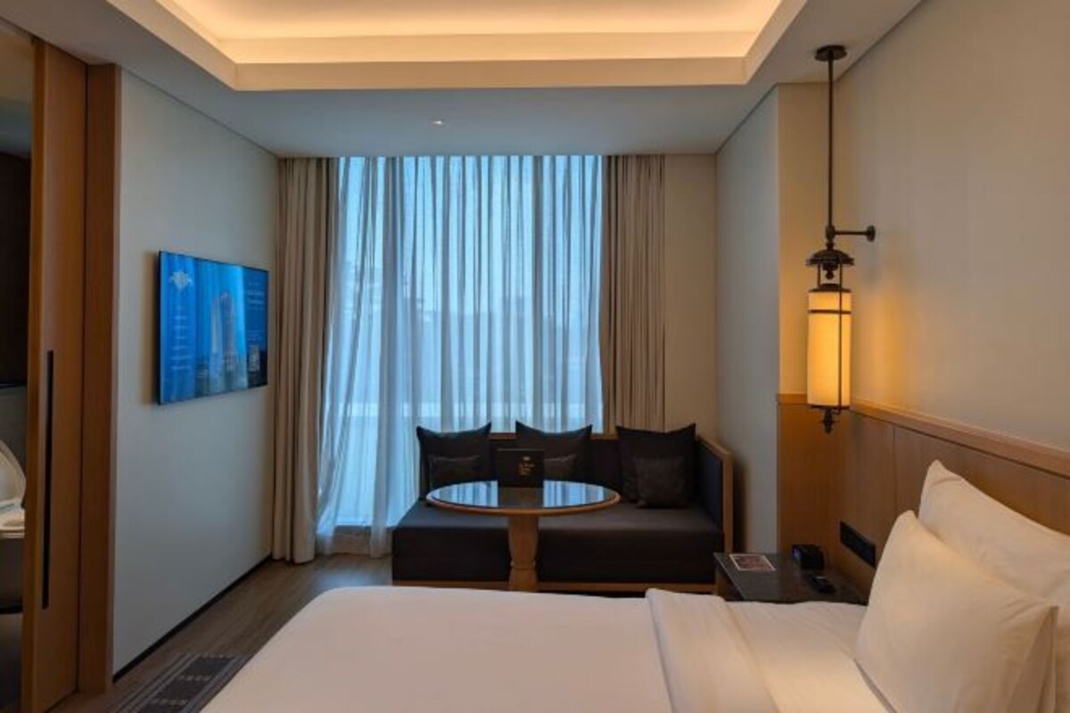 A hotel room with a bed, a round table, a sofa, and a large window with curtains.
