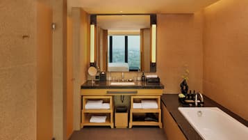 A modern bathroom with a large sink, mirror, and bathtub. It features wooden cabinetry and a view through the window.