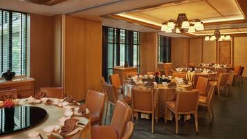 A spacious dining area with multiple round tables, wooden chairs, and a central black table with a decorative centerpiece.