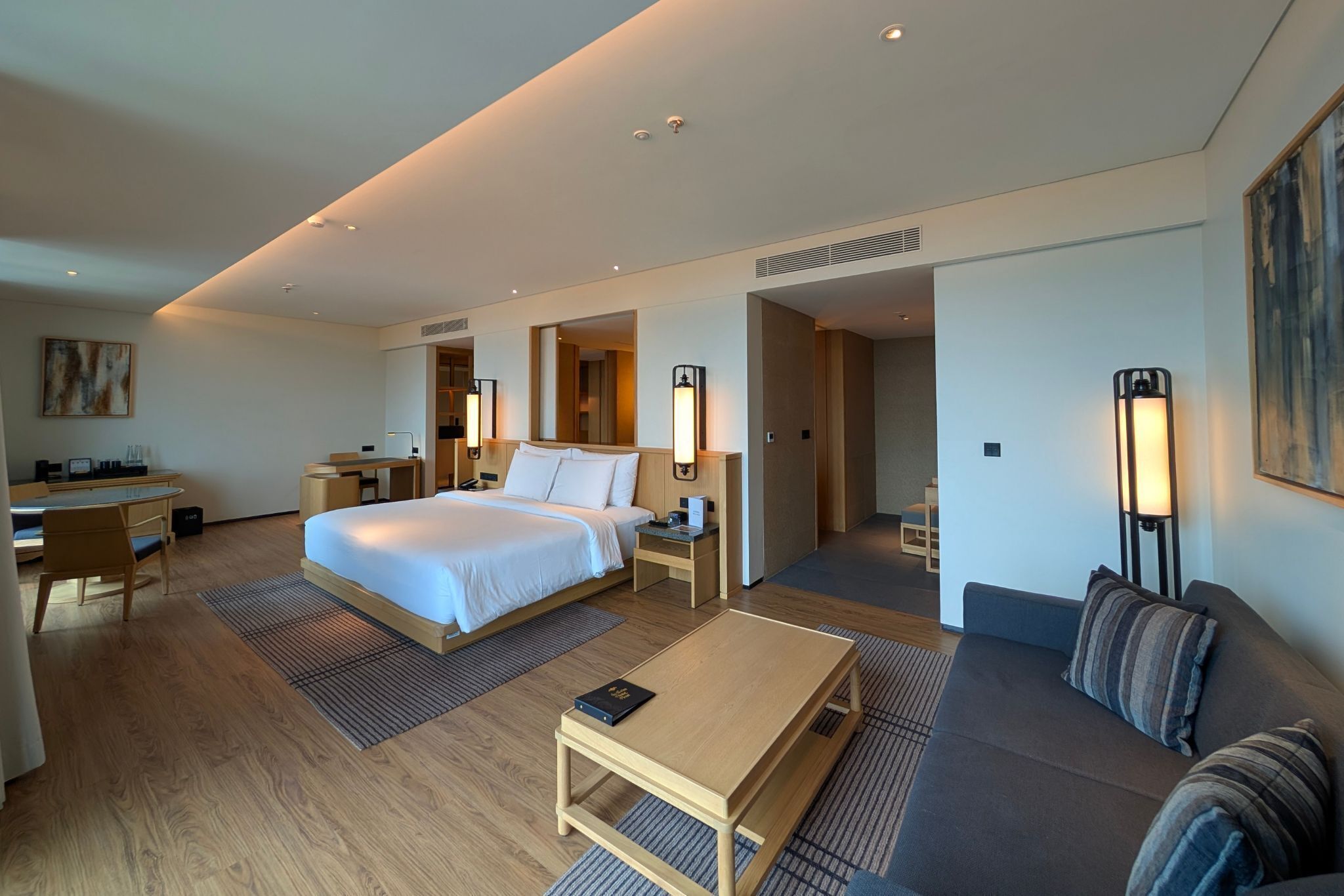 A modern hotel room with a large bed, a desk, a sofa, and a coffee table.