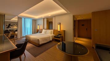 A modern hotel room with a large bed, a desk, a chair, a round table, and a separate seating area.