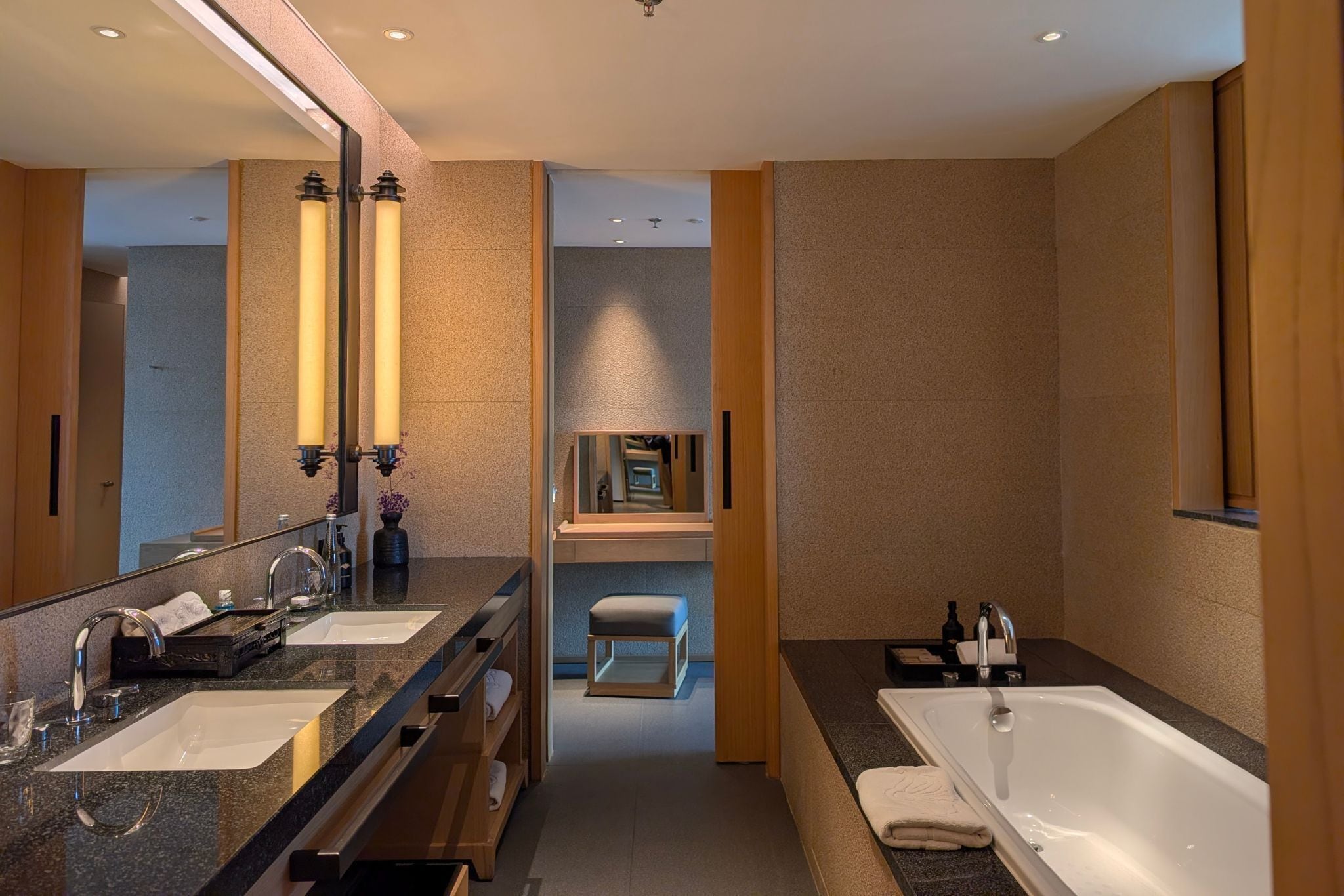 A modern bathroom with dual sinks, a large mirror, a bathtub, and a vanity area.