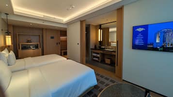 A hotel room with a large bed, a desk, a mirror, and a television displaying a cityscape.