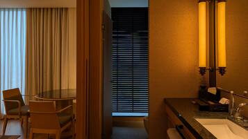 Habitación de hotel con comedor, un ventanal con persianas, un lavamanos y un espejo con apliques de pared.