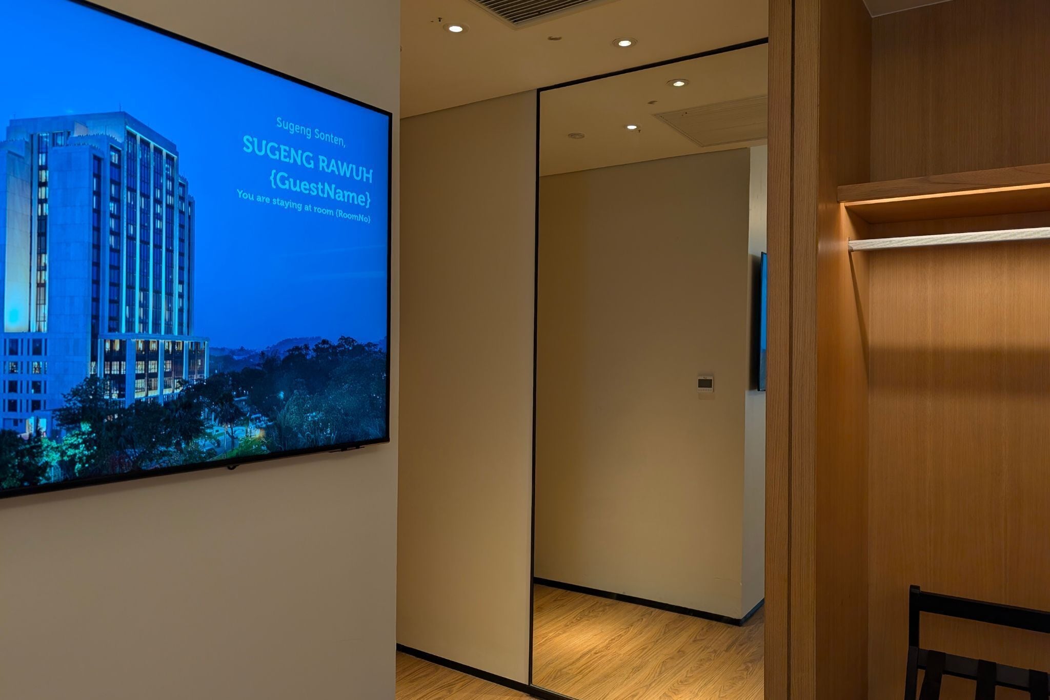 Ein Hotelzimmer mit einem großen digitalen Bildschirm, der eine Stadtansicht und die Zimmernummer des Gastes anzeigt.