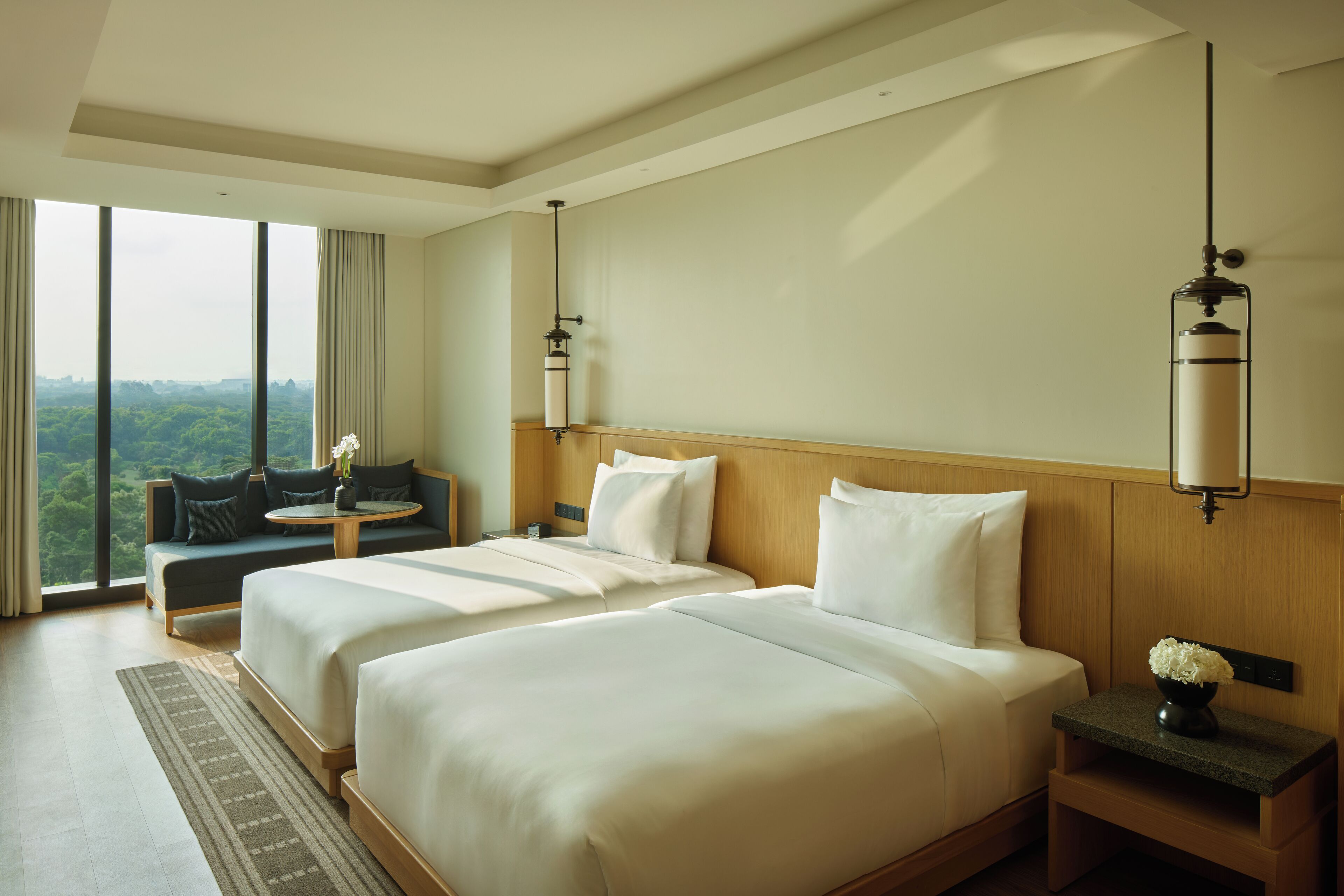 A hotel room with two beds, a sofa, a small table, and a view of the outdoors.