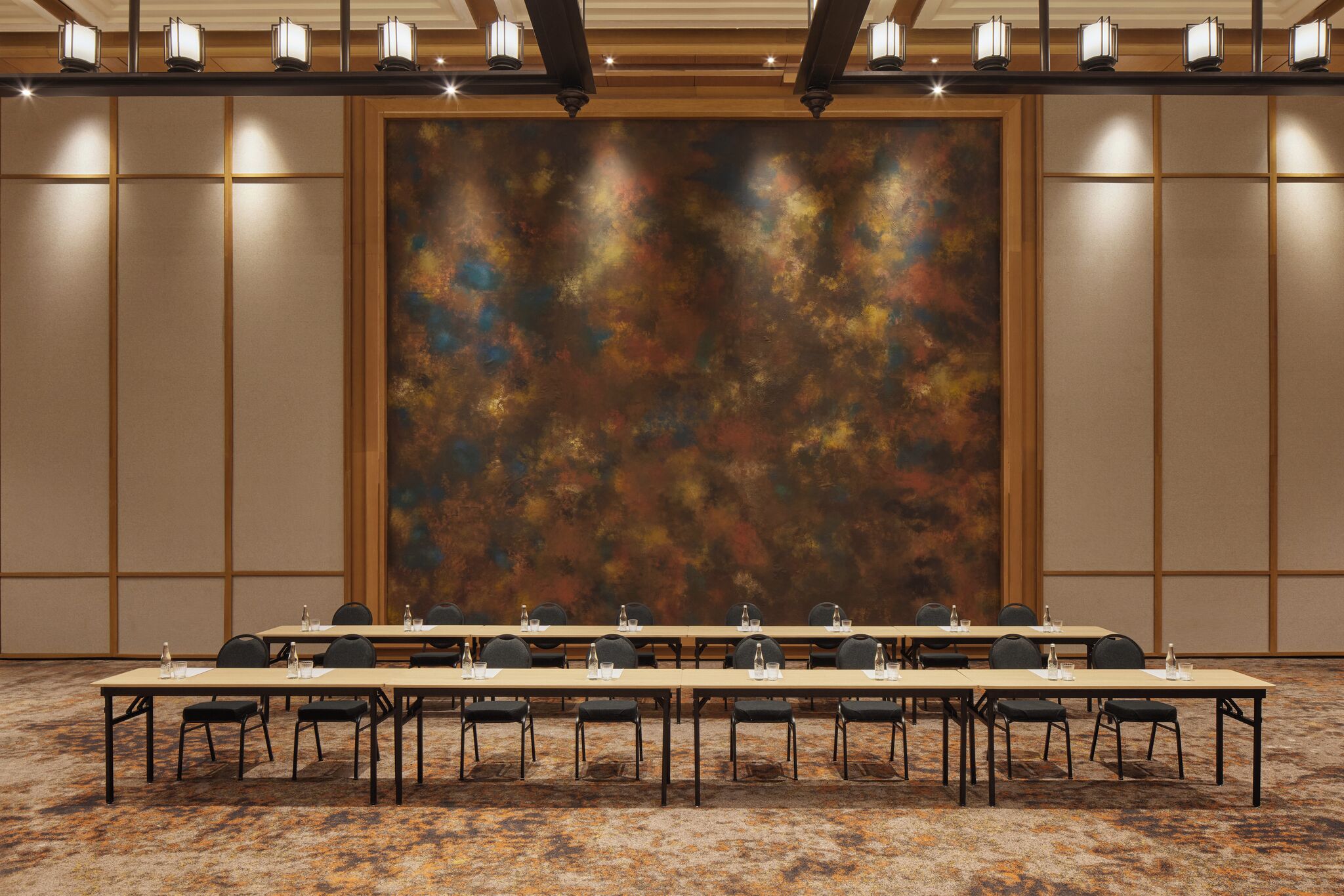 Une salle de conférence avec de longues tables, des chaises et un grand tableau abstrait accroché au mur.