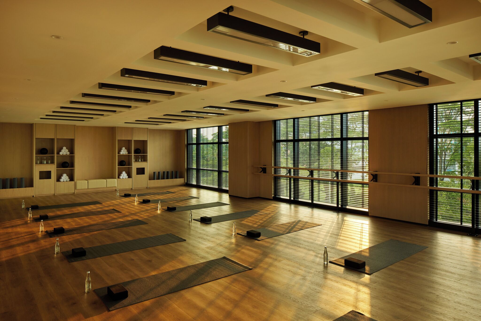 Une pièce spacieuse dotée de grandes fenêtres, d’un plancher en bois et de plusieurs tapis de yoga disposés pour être utilisés.
