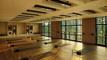 A spacious room with large windows, wooden flooring, and multiple yoga mats arranged for use.