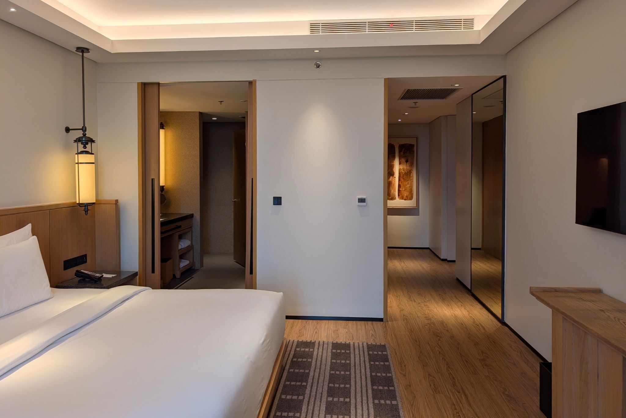 A modern hotel room with a large bed, bedside table, lamp, and a mirror.