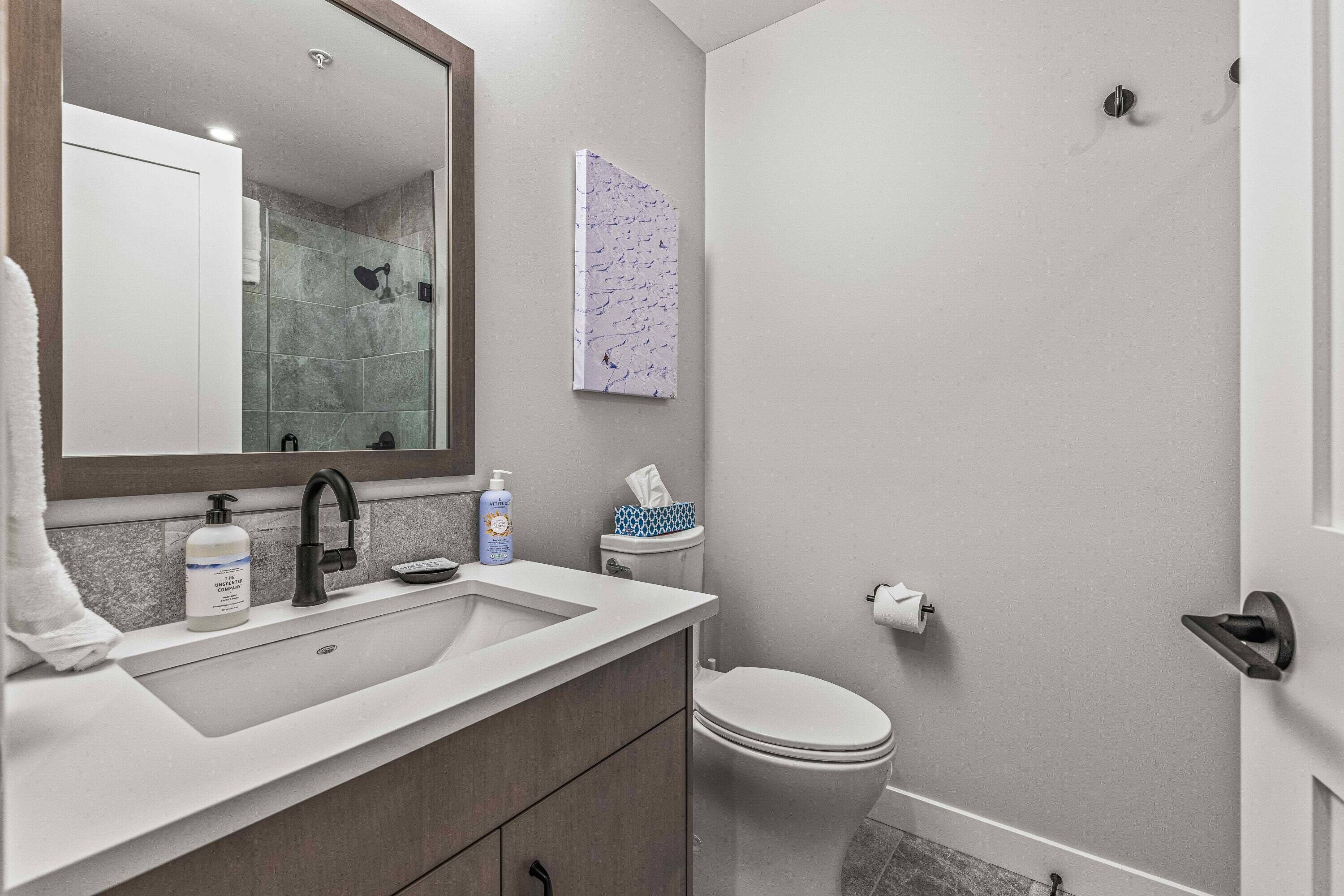 A modern bathroom with a large mirror, a sink with toiletries, a toilet, and a shower area.