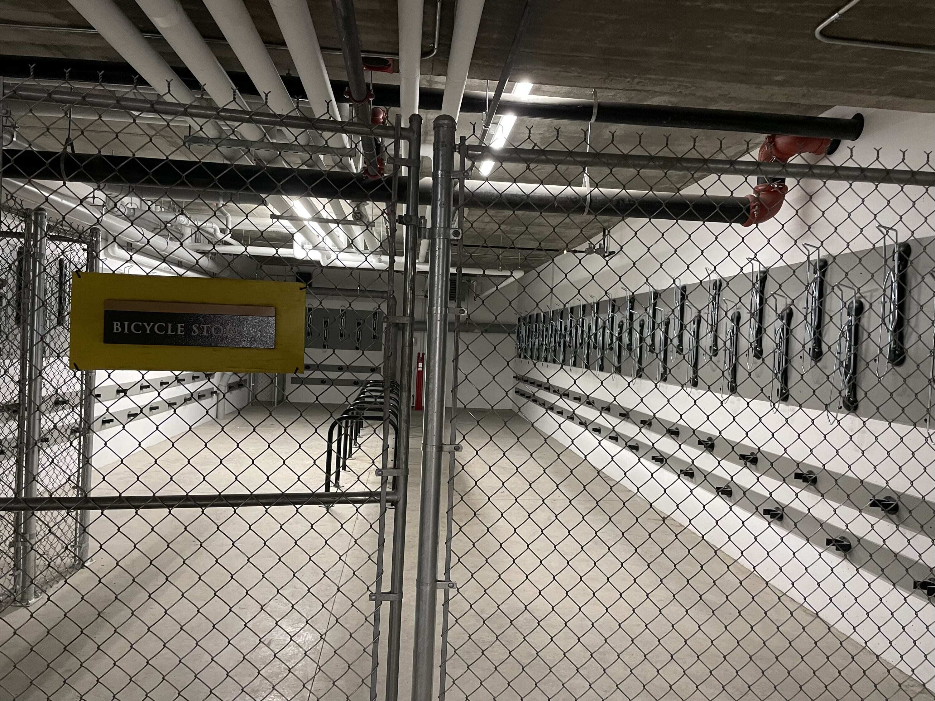 A bicycle storage area with a sign, metal racks, and a concrete floor.