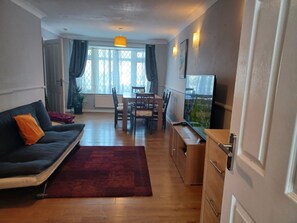Un salon comprenant un canapé, une table à manger avec des chaises, un téléviseur et un coin cuisine.