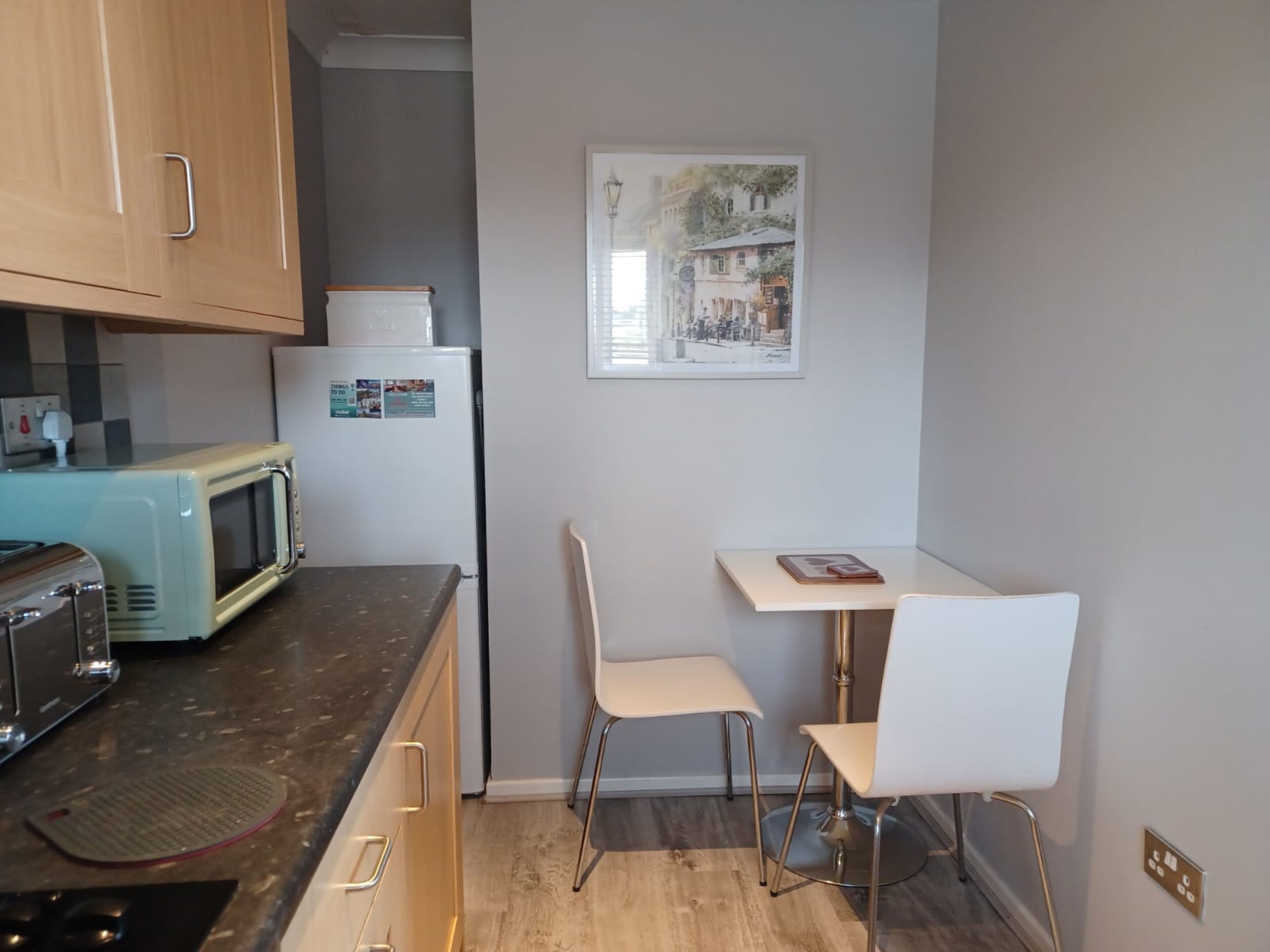 A compact kitchen with a vintage toaster, a refrigerator, and a small dining table with two chairs.